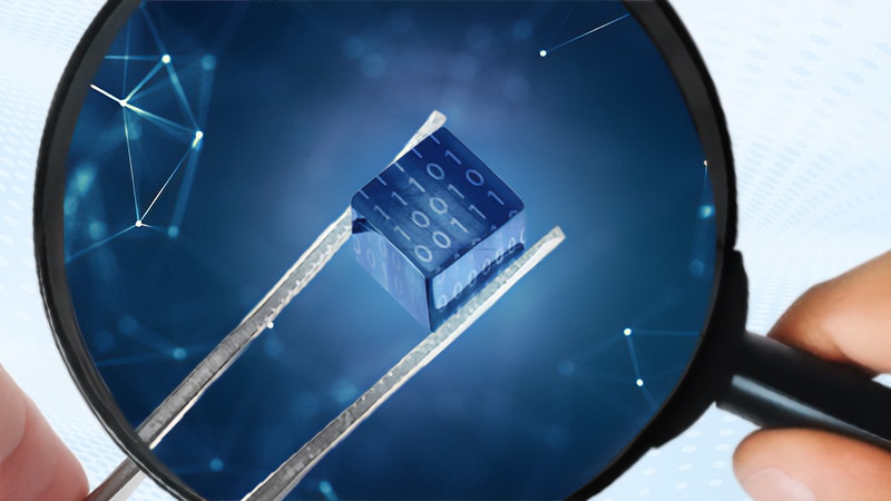 A magnifying glass enlarges a data cube with binary code, held by tweezers, representing data analysis.